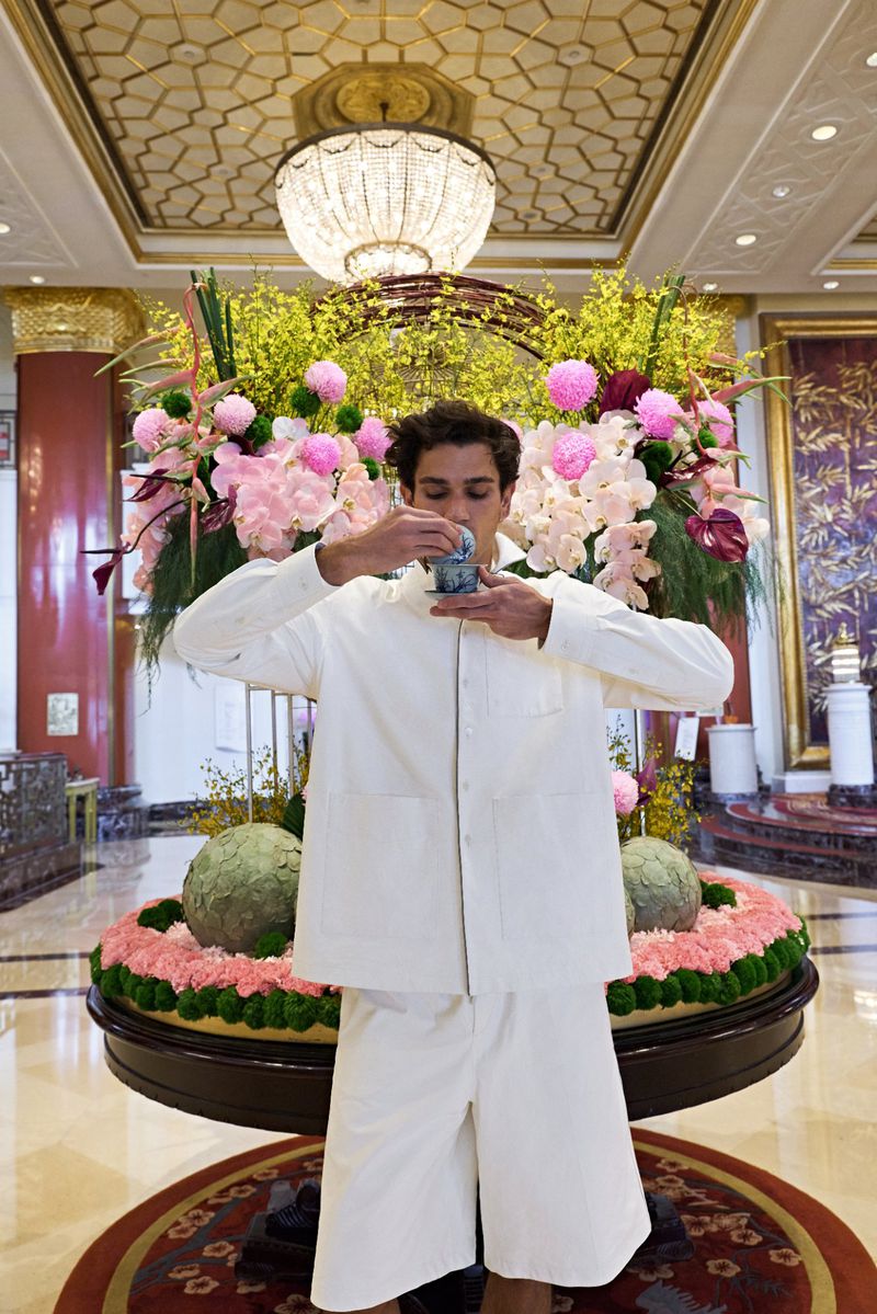 Model in white shirt and shorts holding teacup in luxury hotel lobby for GQ China