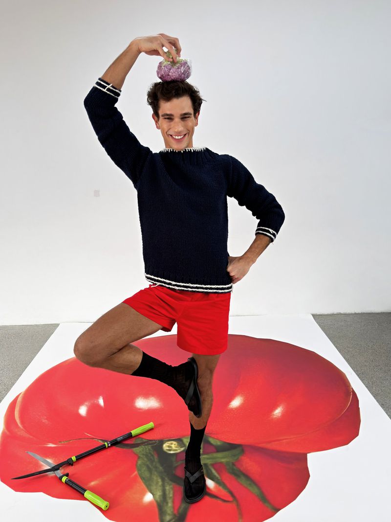 Model balancing a fruit on head while standing on one leg on a large tomato graphic for GQ China