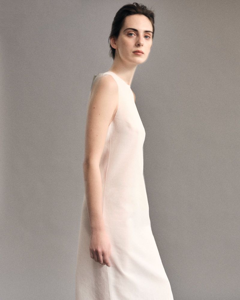Model Lottie Morris wearing a white sleeveless dress against a neutral grey studio backdrop for LUCA FABRY SS26.