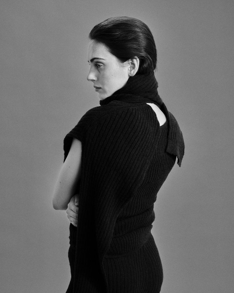 Black and white portrait of a woman wearing a black ribbed turtleneck top against a plain grey seamless background.