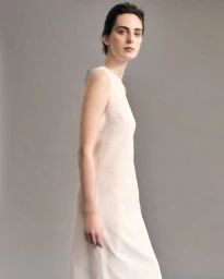 Model Lottie Morris wearing a white sleeveless dress against a neutral grey studio backdrop for LUCA FABRY SS26.