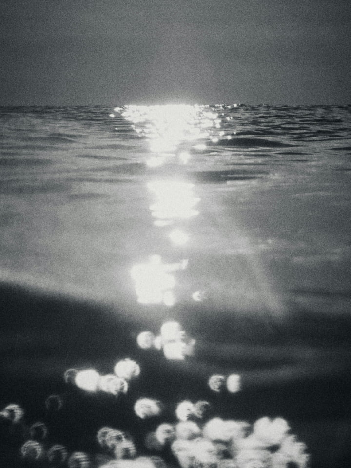 Monochromatic view of sunlight reflecting on ocean water creating shimmering highlights and a somber mood across the water.