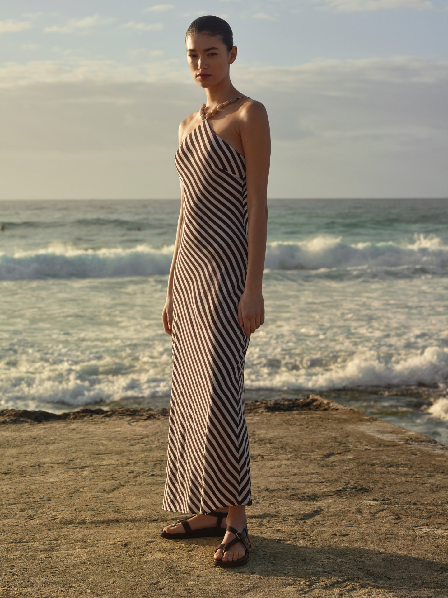 Woman in a striped halterneck dress standing on a coastal platform with the ocean behind her