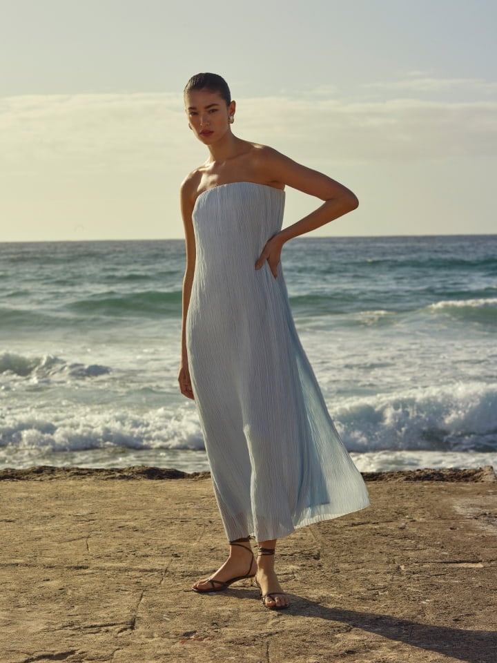 Woman in a long light blue strapless dress posing on a rocky coastline near the ocean for Witchery.