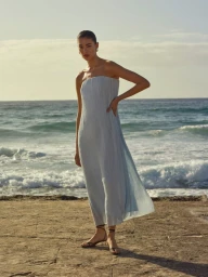 Woman in a long light blue strapless dress posing on a rocky coastline near the ocean for Witchery.