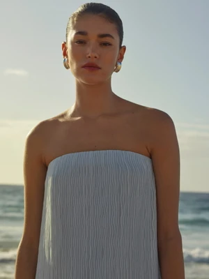 Model wearing a light blue strapless dress and silver earrings against an ocean background