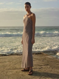 Woman in a striped halterneck dress standing on a coastal platform with the ocean behind her