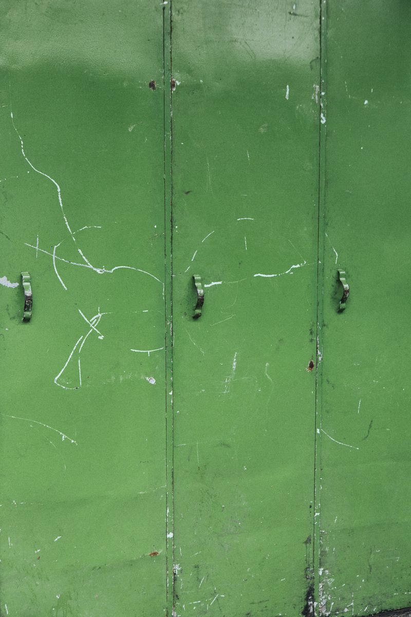 Close-up of weathered green metal industrial garage doors with visible scratches, vertical panels, and small metal handles.