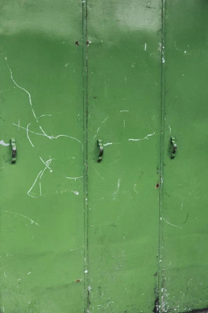 Close-up of weathered green metal industrial garage doors with visible scratches, vertical panels, and small metal handles.