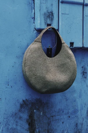 Round metallic textured handbag hanging against a vibrant blue textured wall for The Collector Magazine Bare Walls project.
