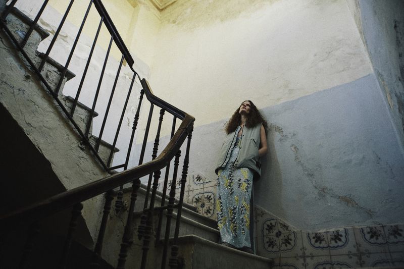 Model standing on a staircase leaning against a weathered wall for The Collector Magazine editorial