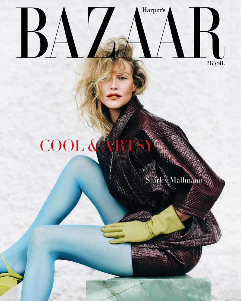 Shirley Mallmann poses for Harper's Bazaar Brasil, wearing a glossy burgundy jacket and skirt, matched with bright blue hosiery and green gloves.