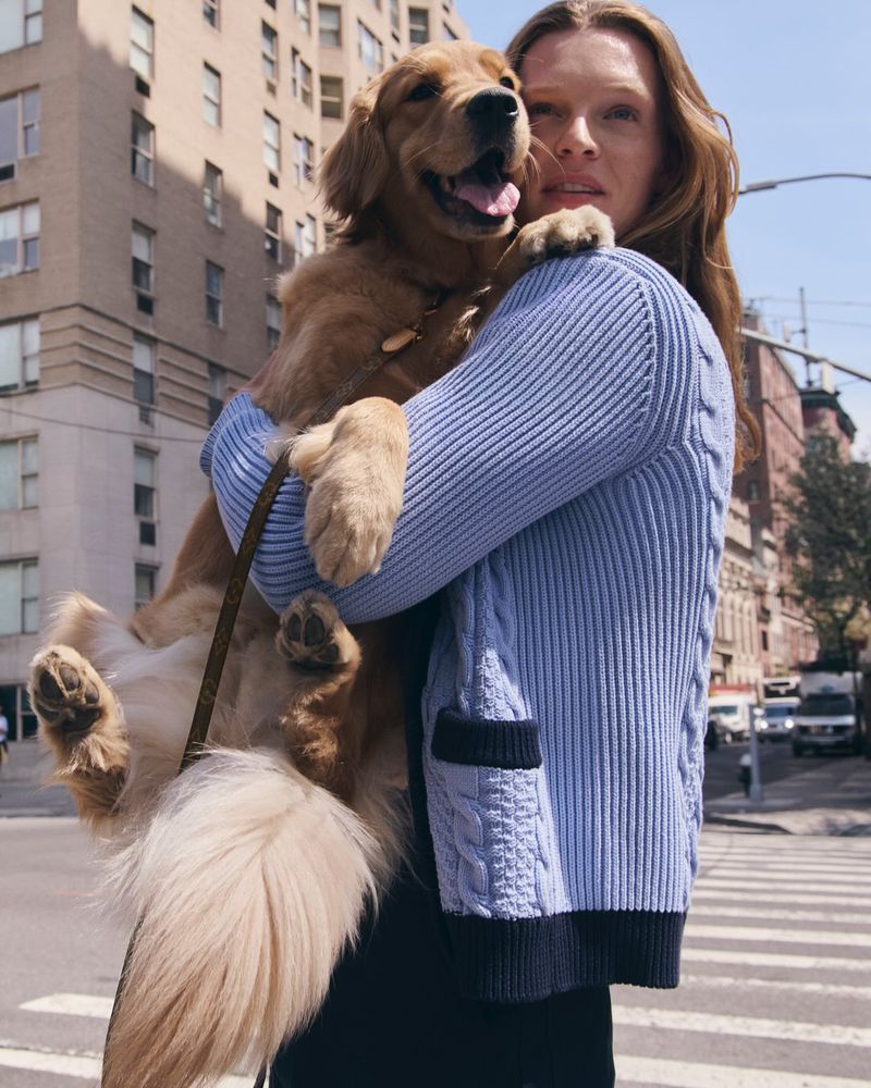 Woman in blue knitted cardigan holding a golden retriever dog on a city street