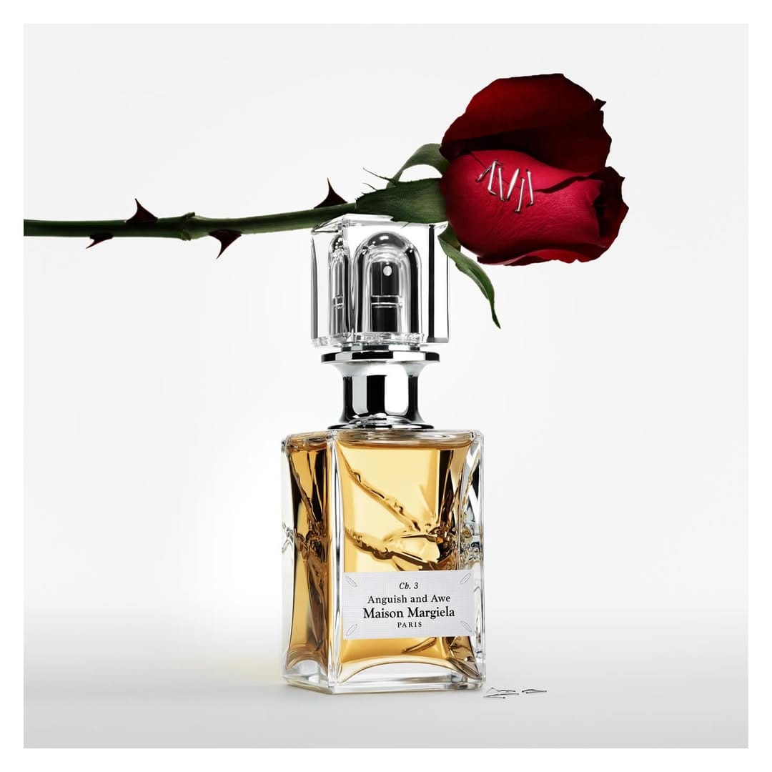 Crystal perfume bottle with amber liquid topped by a red rose on a white seamless background for Maison Margiela.