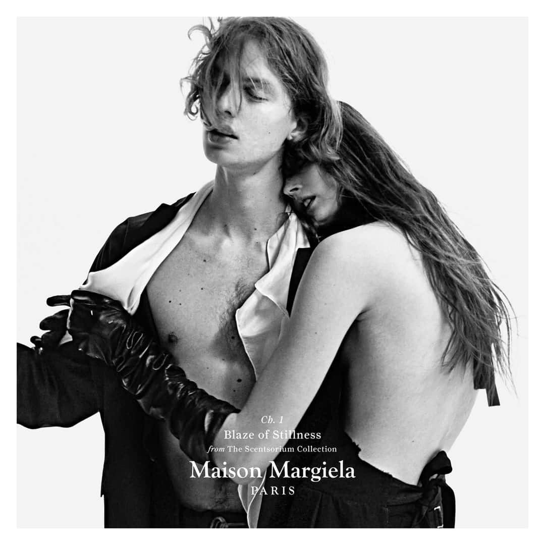 Black and white fashion campaign image featuring two models embracing against a seamless white background for Maison Margiela.