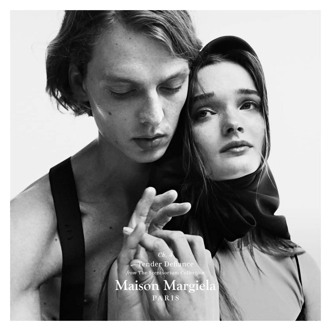 Close-up monochrome portrait of two models embracing, hands entwined, with Maison Margiela Paris typography.