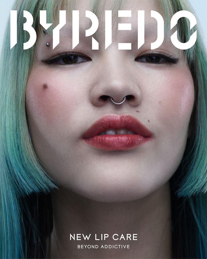 Close-up of an Asian adult female model with green-blue hair and red lipstick, against a light background for a beauty ad.