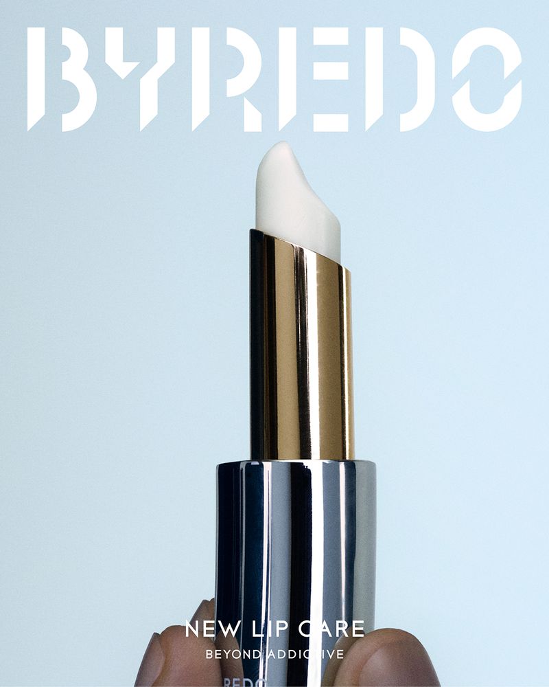 Lip balm stick in silver and gold casing with visible product; beauty and self-care product shot against a light blue backdrop.