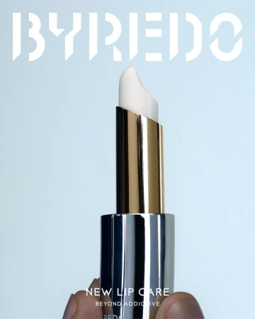 Lip balm stick in silver and gold casing with visible product; beauty and self-care product shot against a light blue backdrop.