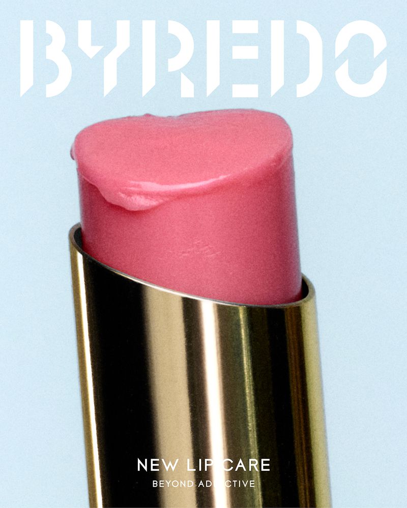 Close-up of Byredo lip balm with gold tube and pink balm against a pale blue background. Features Byredo logo and text 'New Lip Care'.