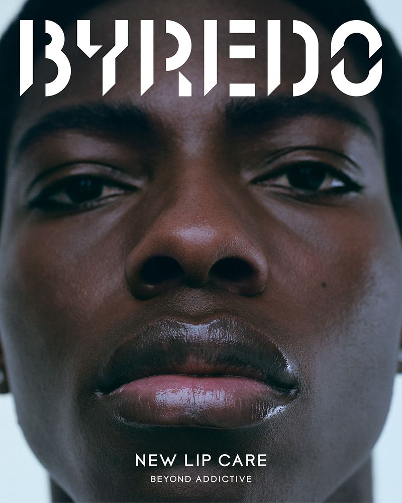 Close-up portrait of an African American adult woman with glossy lips, promoting new lip care product by Byredo, dark color palette.