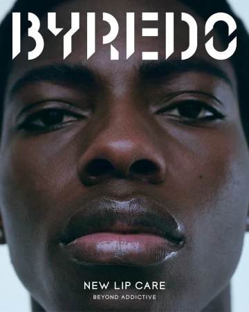 Close-up portrait of an African American adult woman with glossy lips, promoting new lip care product by Byredo, dark color palette.