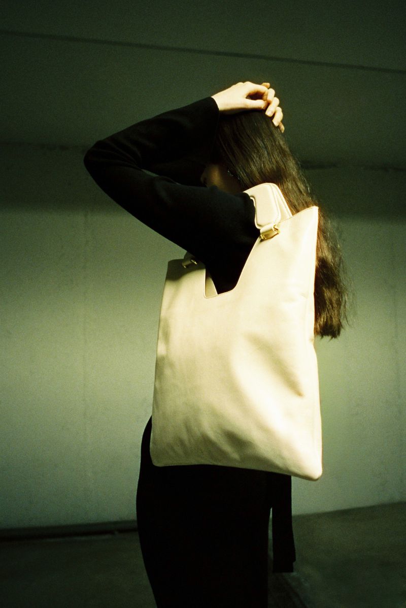 A person wearing a black long-sleeved shirt with a cream-colored tote bag over their shoulder, with a focus on fashion and style.
