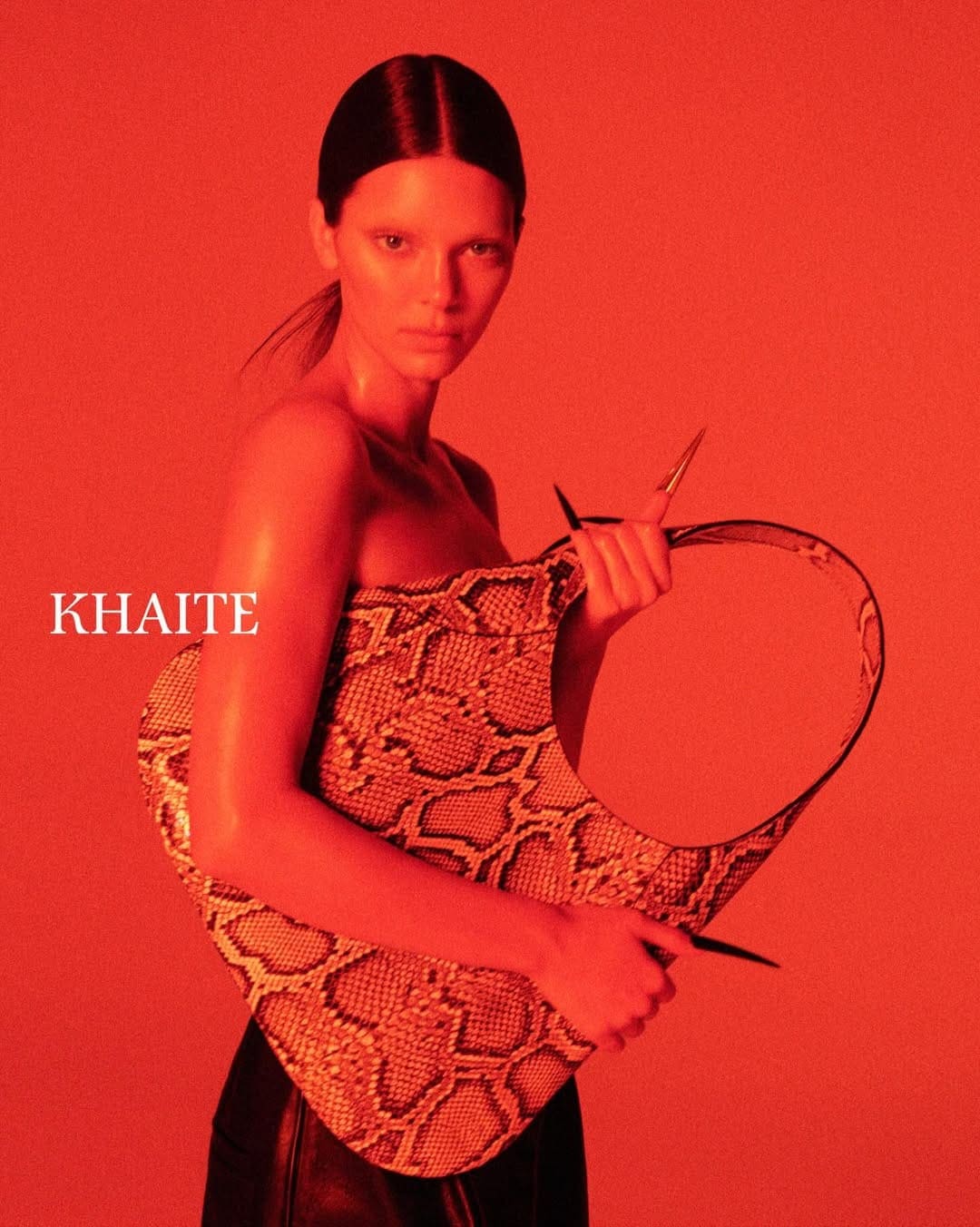 Kendall Jenner holding a snakeskin handbag against a monochromatic red studio background for Khaite Spring 2026 ad campaign.