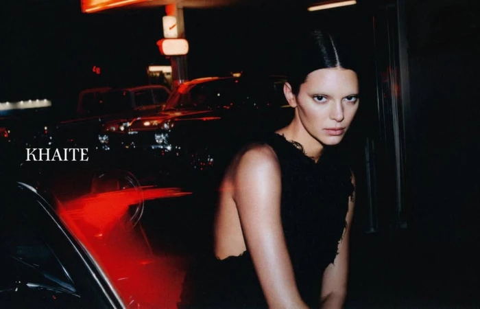 Model Kendall Jenner wearing a black top at night with cars and red neon lighting in the background for Khaite Spring 2026 ad campaign.