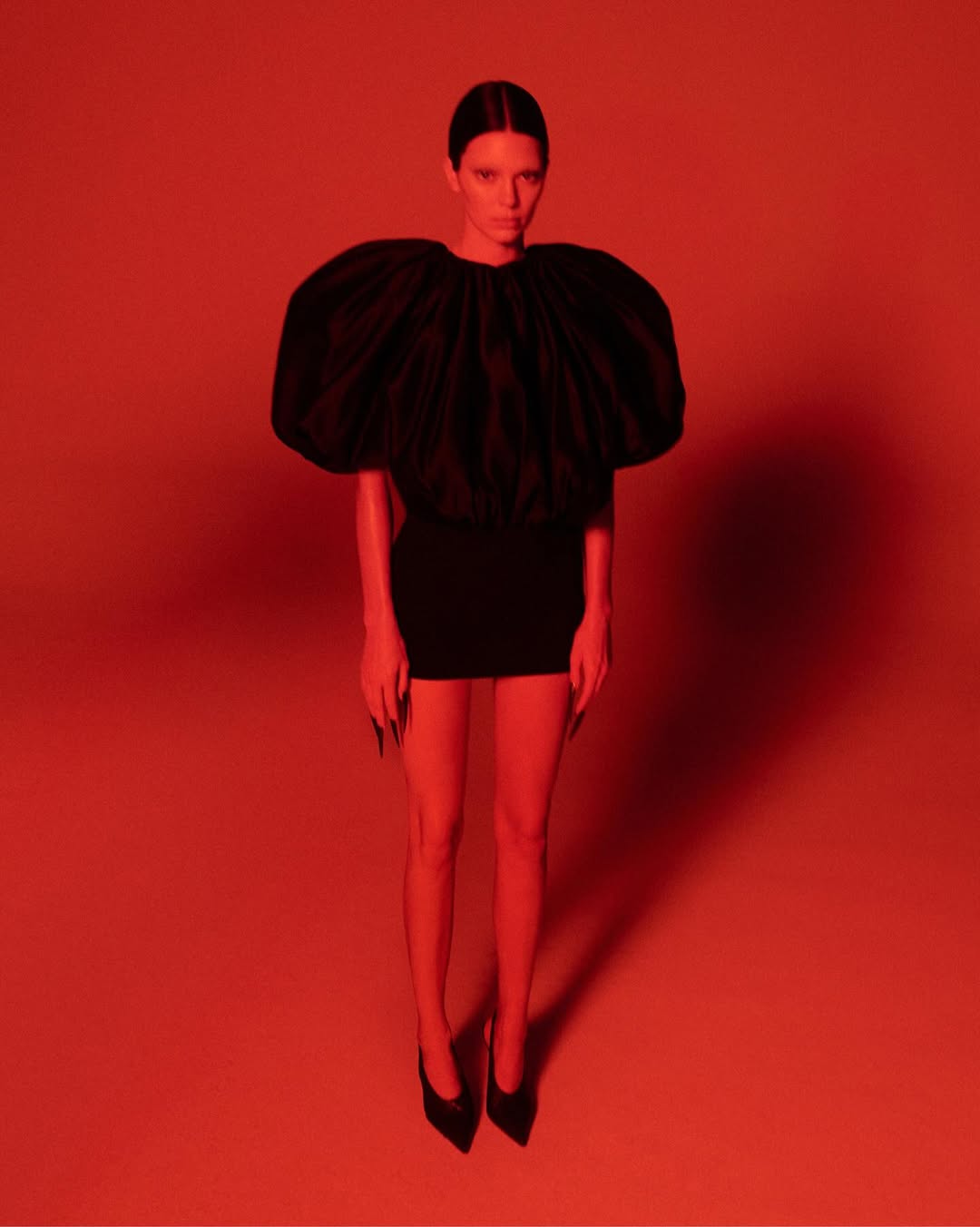 Model Kendall Jenner wearing a black puff-sleeve top and mini dress under dramatic red lighting for Khaite Spring 2026 ad campaign.