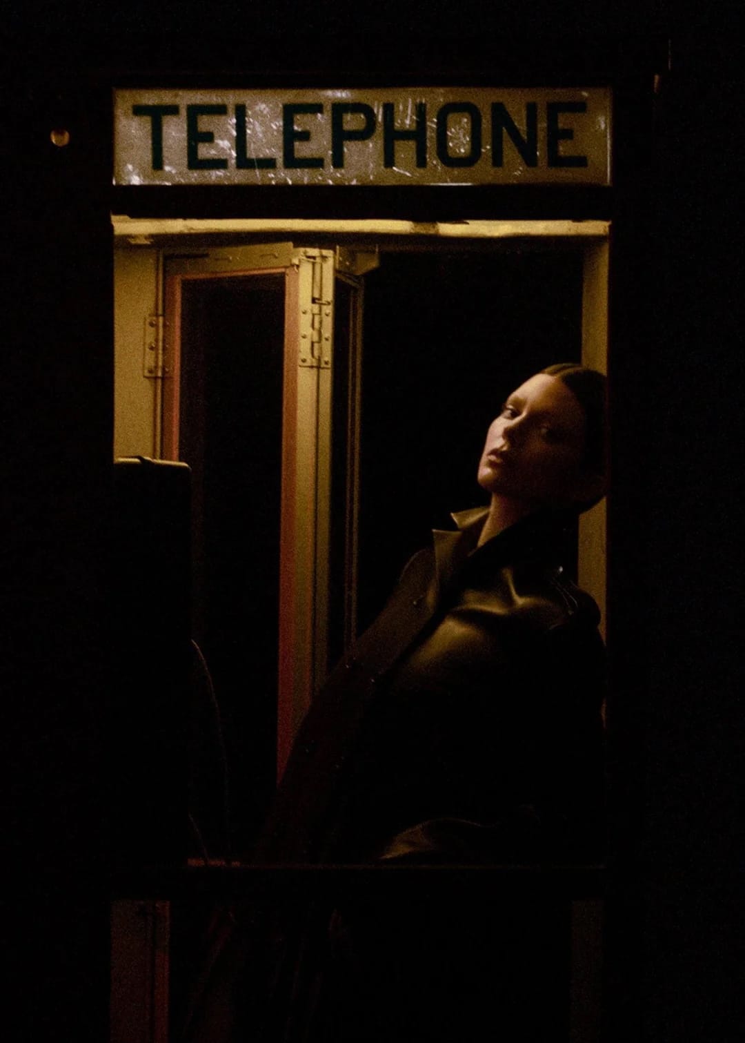 Model Kendall Jenner standing inside a dimly lit telephone booth at night for Khaite Spring 2026 Ad Campaign