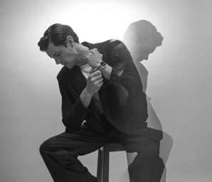 Model Lewis Jamison seated on a stool wearing a black suit jacket and stainless steel watch with a double exposure silhouette.