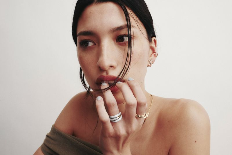 Close-up portrait of a woman wearing rings and ear cuffs against a seamless background for a Mejuri campaign.