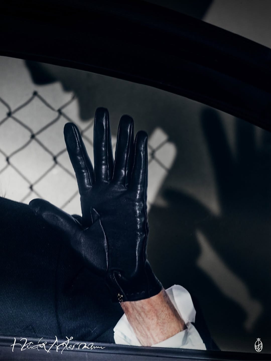Close-up of a gloved hand pressing against a car window with a chain-link fence shadow cast in the background.