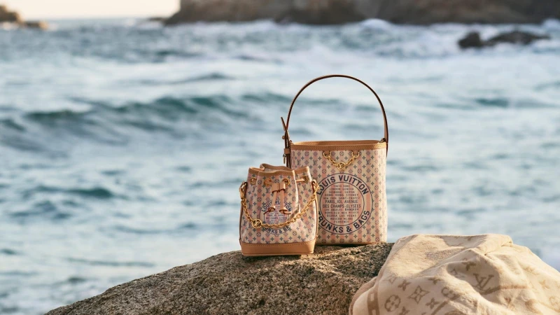 Two Louis Vuitton monogram canvas bucket bags resting on a rocky shore beside the ocean