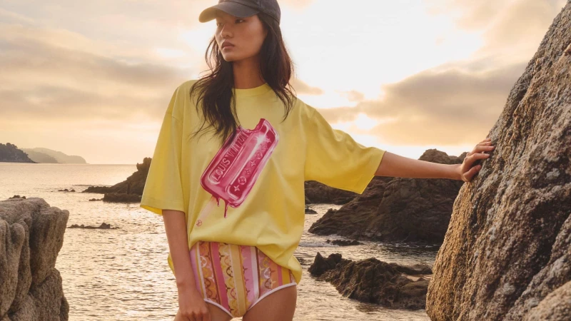 Model wearing a yellow t-shirt and patterned shorts standing by rocky coast at sunset for Louis Vuitton