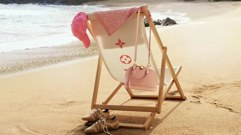 Louis Vuitton deck chair on a sandy beach featuring a pink handbag, matching baseball cap, towel, and sneakers.