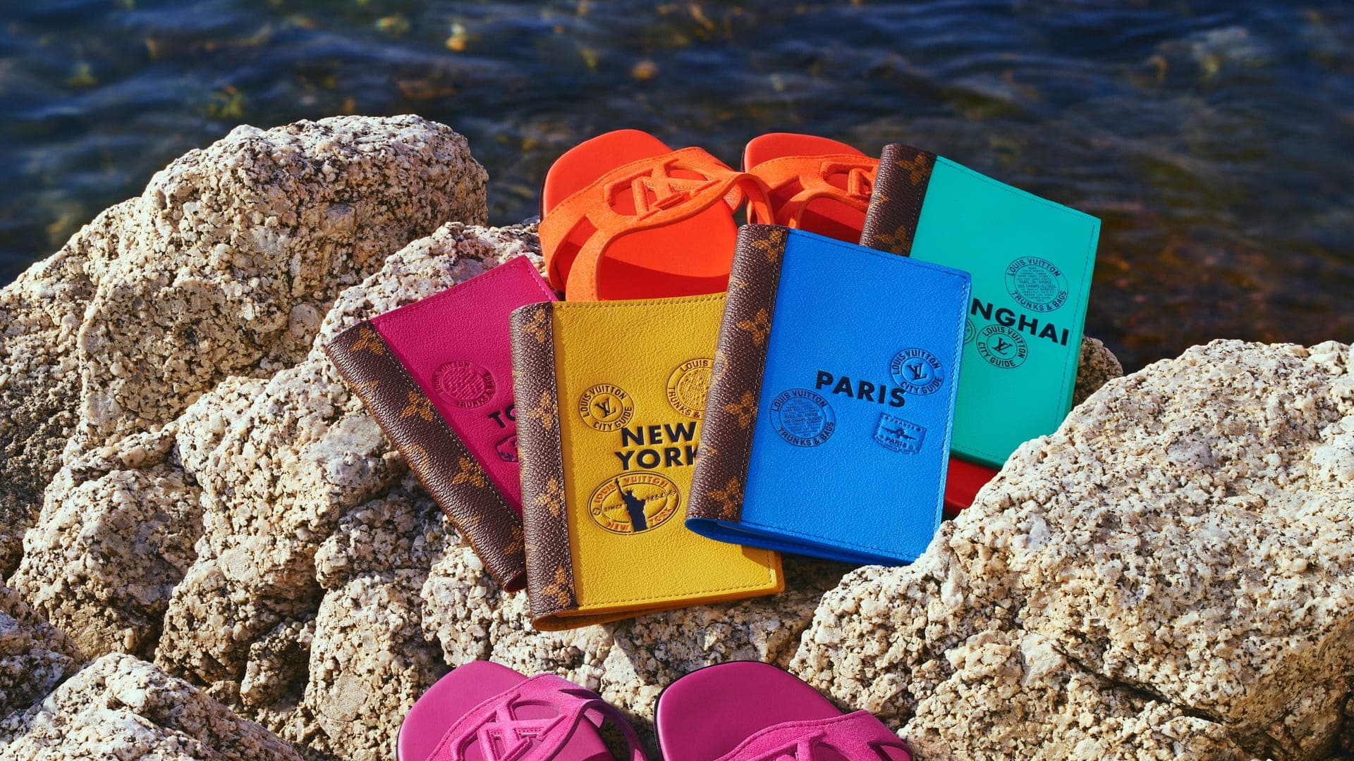 Colorful leather city guides and designer sandals arranged on rough coastal rocks near water