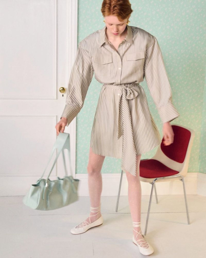 Model in striped shirt dress holding a light blue shoulder bag in an interior setting for & Other Stories.