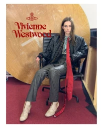 Model seated in black office chair wearing a black quilted jacket and red tie for Vivienne Westwood fall/winter 2025 campaign.
