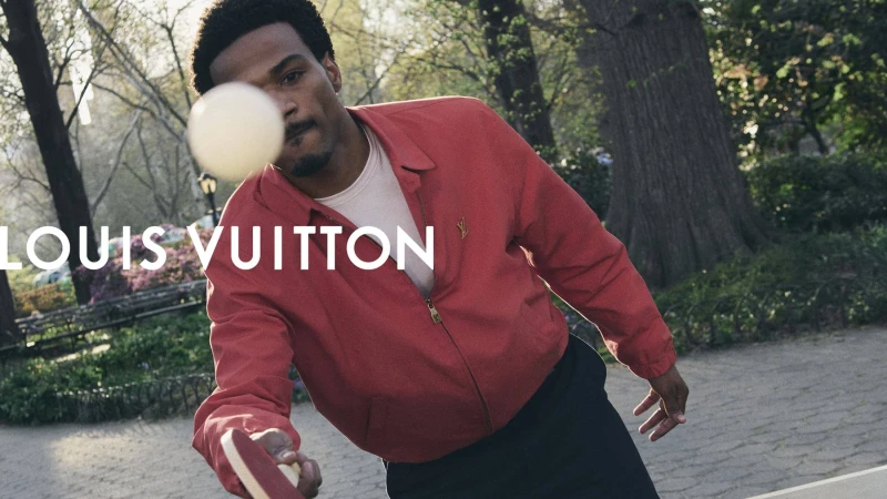 Tyshawn Jones playing table tennis wearing a red zip-up jacket in a park setting for Louis Vuitton.
