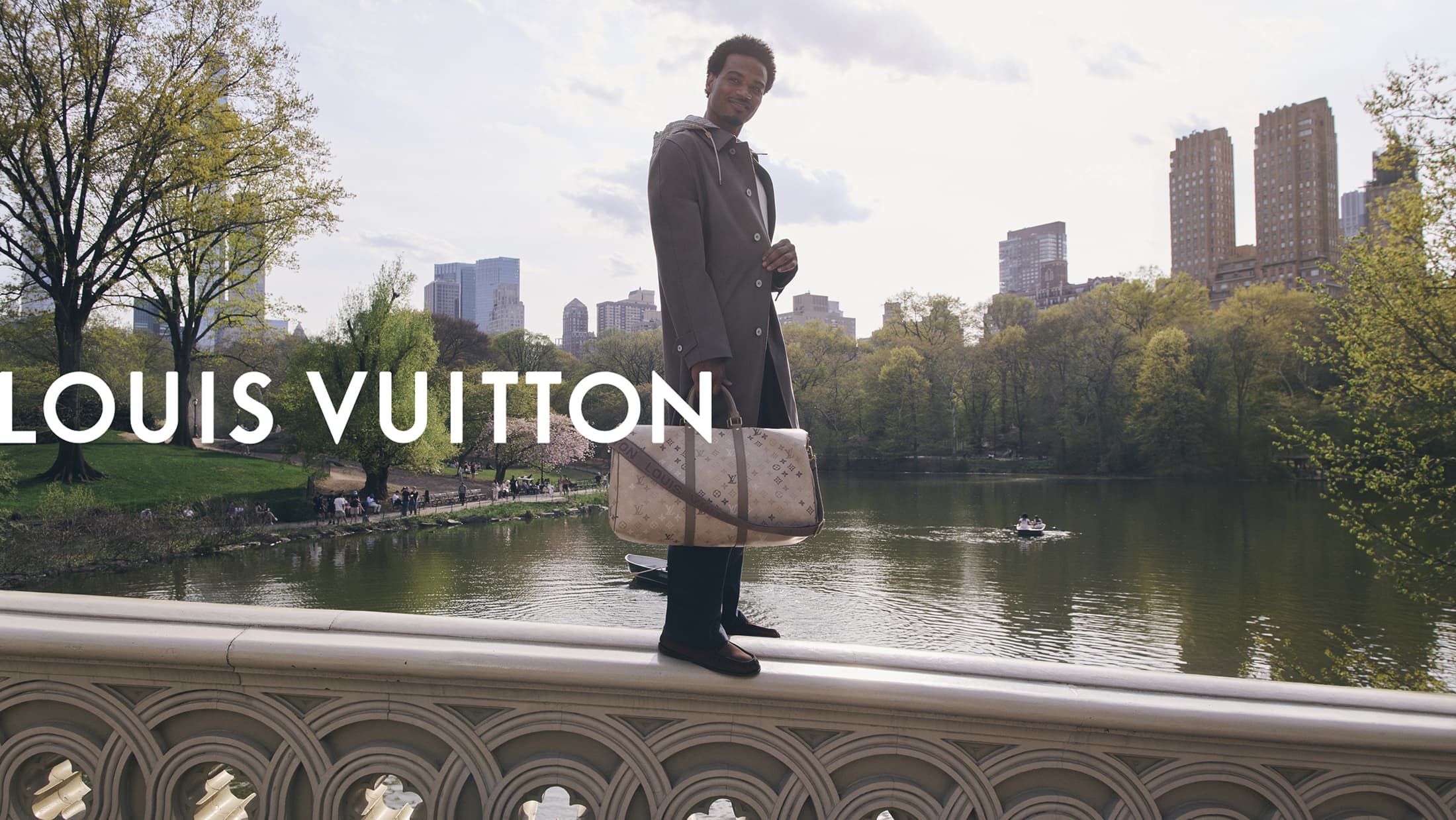 Tyshawn Jones standing on a stone bridge holding a Monogram duffle bag for Louis Vuitton in New York City.