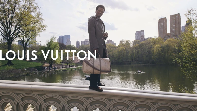 Tyshawn Jones standing on a stone bridge holding a Monogram duffle bag for Louis Vuitton in New York City.