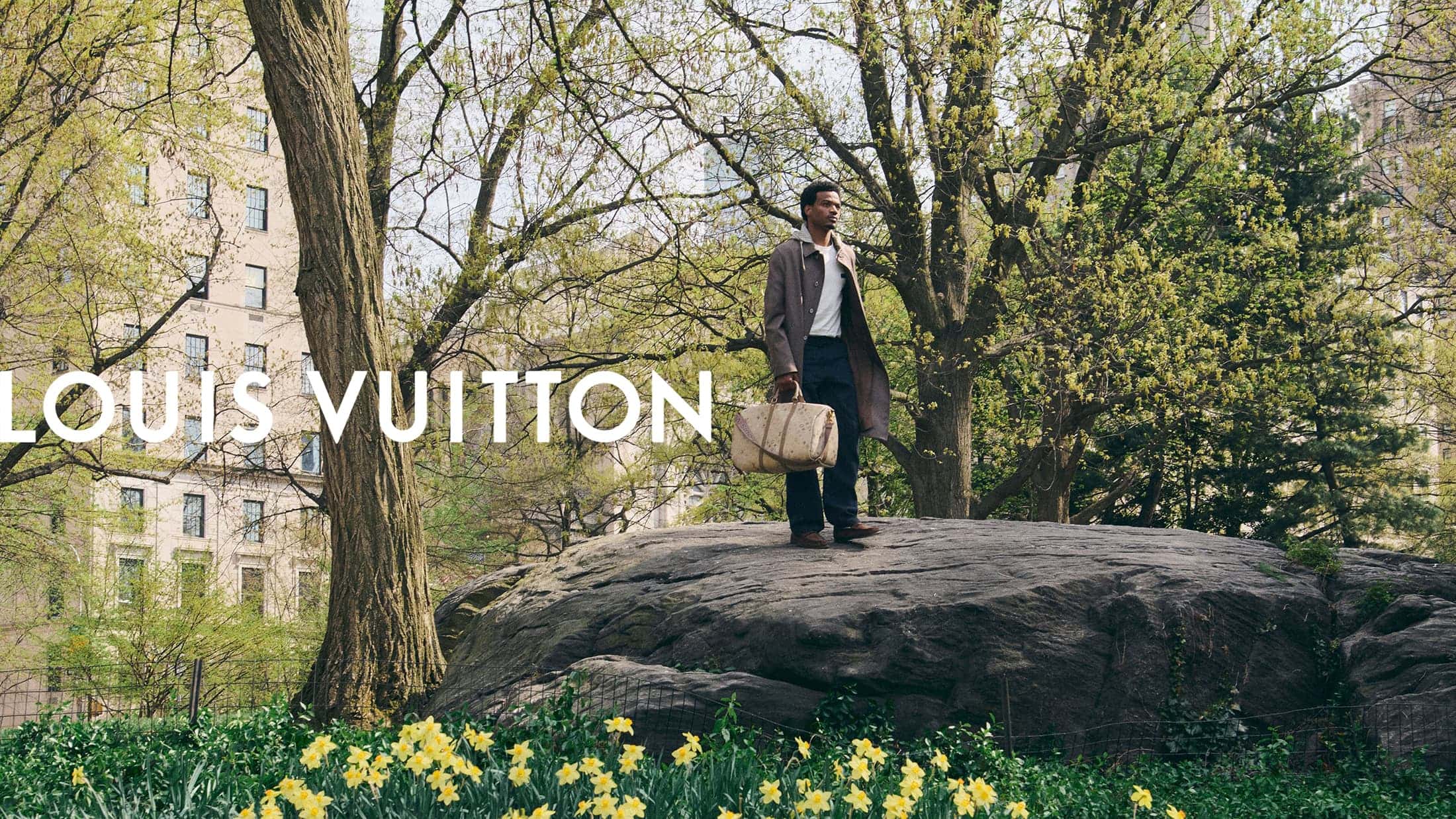 Tyshawn Jones standing on a large rock in Central Park carrying a Louis Vuitton travel bag for the Pre-Fall 2026 campaign.