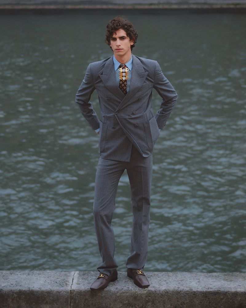 A man in a grey suit standing on a stone ledge beside water for GQ Turkey photographed by Ben Bortis.