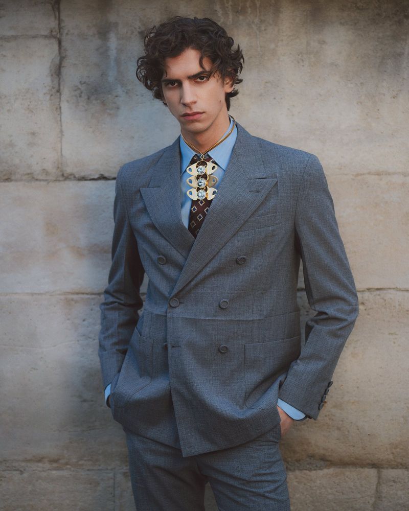 Model Hedi Ben Tekaya in a grey double-breasted suit standing against a textured stone wall for GQ Turkey Homme D'Ailleurs