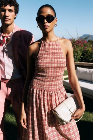 Woman in red patterned halter dress holding white handbag standing beside man outdoors in sunny light
