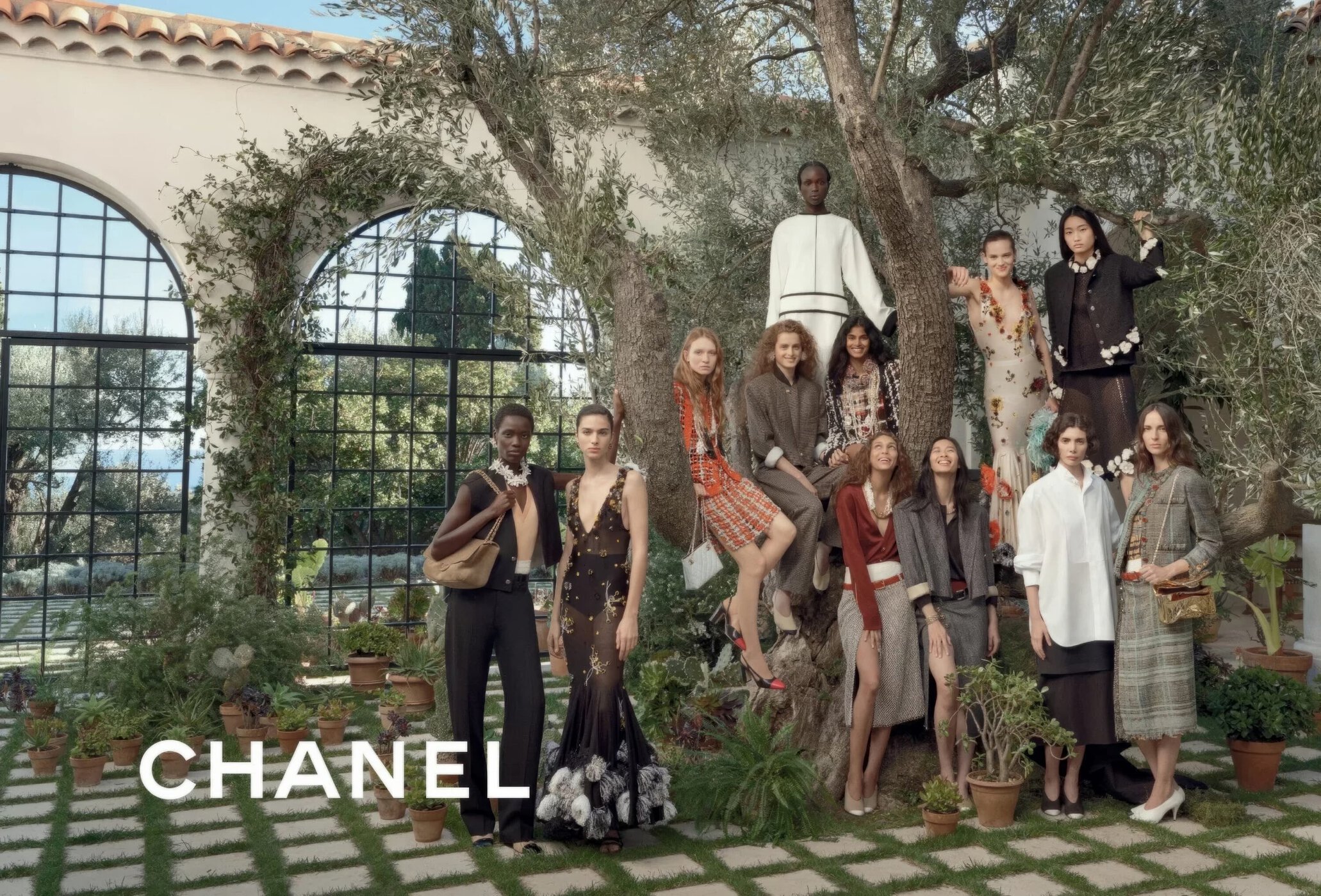 Group of female models in Chanel spring collection posing outdoors among olive trees and arched windows