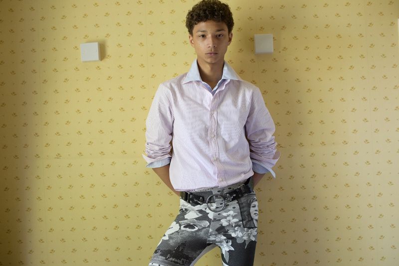 Young male model wearing striped shirt and patterned trousers standing against yellow wallpaper