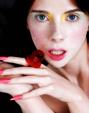 Close-up portrait of a woman with frosted face makeup and pink lips holding a bright red ring pop candy.